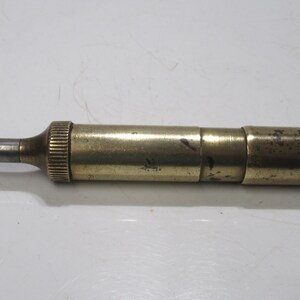 May include: A vintage brass telescope with a silver eyepiece. The cylindrical telescope has a ribbed section near the eyepiece and a slightly tarnished finish. It is lying horizontally on a white surface.