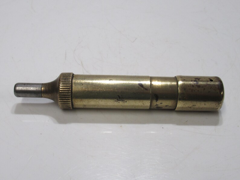 May include: A vintage brass telescope with a silver eyepiece. The cylindrical telescope has a ribbed section near the eyepiece and a slightly tarnished finish. It is lying horizontally on a white surface.