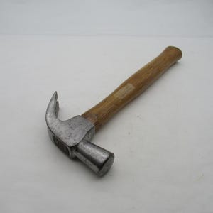 May include: A claw hammer with a wooden handle and a silver-coloured head. The hammer is angled, showing the claw and the striking face. The handle is a light brown colour.