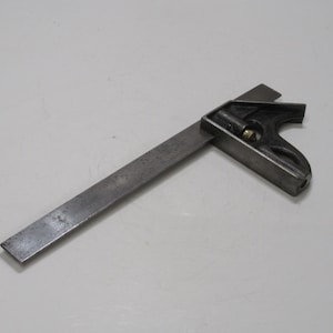 May include: A combination square tool, with a dark grey head and a silver blade. This tool is used for measuring and marking angles, and is common in woodworking and metalworking. The blade is approximately 20 cm long.