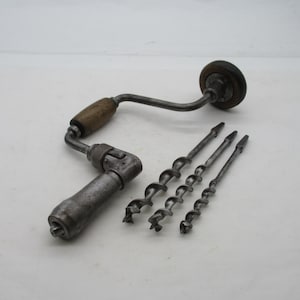 May include: A vintage metal hand brace drill featuring a wooden handle and a rotating knob, accompanied by three distinct steel auger drill bits of varying sizes, all displaying a weathered, metallic finish and signs of past use.