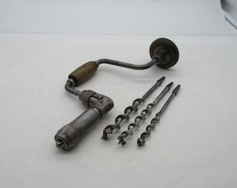 May include: A vintage metal hand brace drill featuring a wooden handle and a rotating knob, accompanied by three distinct steel auger drill bits of varying sizes, all displaying a weathered, metallic finish and signs of past use.