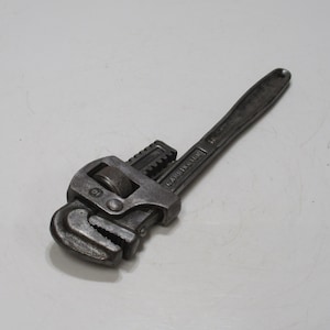 May include: A grey adjustable pipe wrench. The wrench features a textured handle and an adjustable jaw controlled by a knurled wheel. This metal tool is likely used for plumbing or mechanical tasks.