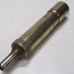 May include: A vintage brass and steel tool with a cylindrical body. The tool has a ribbed grip section and a tapered nozzle. The metal has a worn, aged appearance.