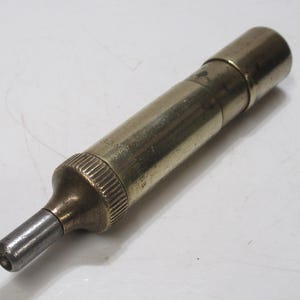 May include: A vintage brass and steel tool with a cylindrical body and a tapered tip. The tool has a knurled grip and appears to be a precision instrument, possibly for measuring or adjusting. The metallic finish gives it an antique appearance.