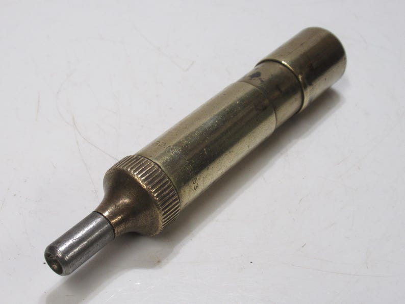 May include: A vintage brass and steel tool with a cylindrical body and a tapered tip. The tool has a knurled grip and appears to be a precision instrument, possibly for measuring or adjusting. The metallic finish gives it an antique appearance.