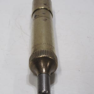 May include: A cylindrical brass object with a silver-coloured tip. The object has a ridged base and a slightly darker top. The text "RC NO. 715853" is visible on the side. The object is likely a tool or instrument.