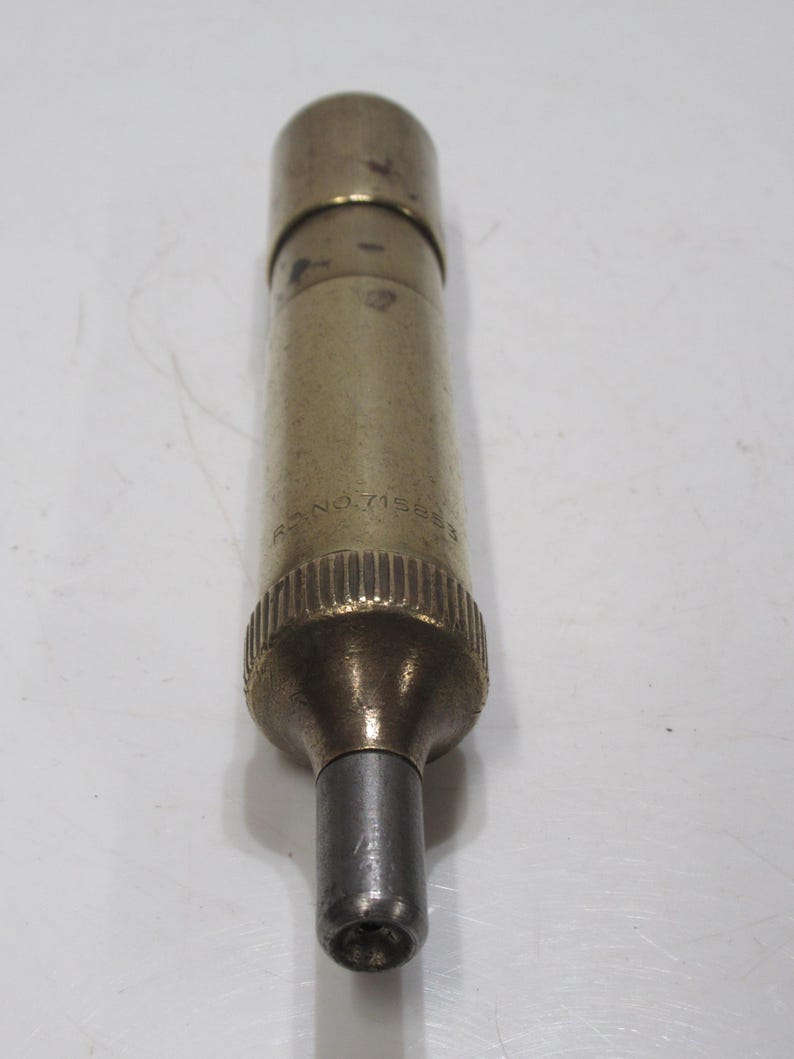 May include: A cylindrical brass object with a silver-coloured tip. The object has a ridged base and a slightly darker top. The text "RC NO. 715853" is visible on the side. The object is likely a tool or instrument.