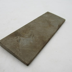 Peut inclure: Une pierre à aiguiser rectangulaire de couleur gris-brun. La pierre a une texture légèrement rugueuse et est conçue pour l'affûtage des lames. La pierre mesure environ 20 cm de long et 5 cm de large.