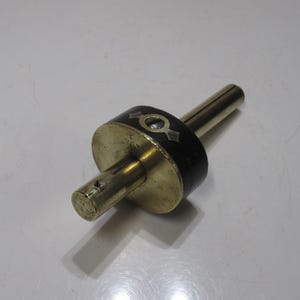 May include: A brass marking gauge with a black band and decorative inlays. The gauge has a cylindrical body and a long, slender rod extending from one end. The tool is designed for woodworking and marking precise measurements.