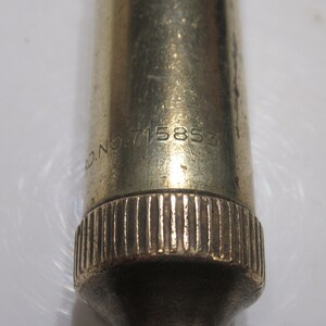May include: Close-up of a vintage brass object with the text "D.NO. 715853" engraved on its surface. The object has a ridged base and a slightly tarnished appearance, suggesting age and use.
