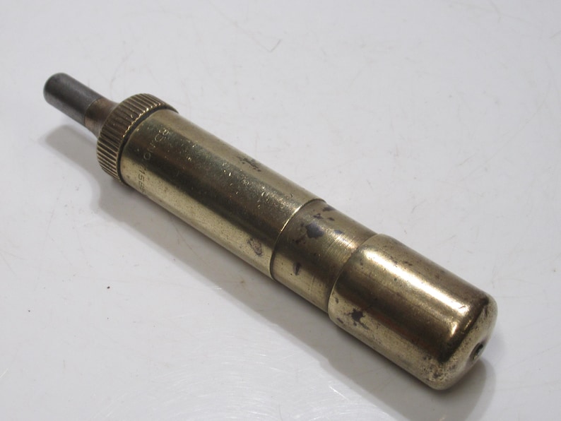 May include: A vintage brass tool with a cylindrical body and a knurled grip. The tool has a dark metal tip and a rounded end. The brass has a tarnished appearance, suggesting age and use. The tool is likely used for a specific mechanical purpose.