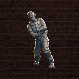 May include: A gray, detailed figurine of a zombie wearing a straitjacket and standing on a brick wall background.