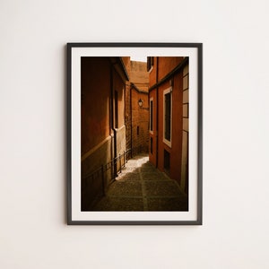 May include: A narrow, cobblestone alleyway in a European city. The walls are a warm, orange-brown color, and the alley is lit by a single street lamp.