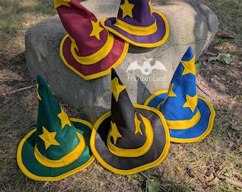 Puede incluir: Cinco sombreros de mago puntiagudos en morado, granate, verde, negro y azul, cada uno con aplicaciones de estrellas amarillas y un borde amarillo. Los sombreros están etiquetados como pequeños de 53,34 cm. Se ve un logo con el texto Fruitbat Land.