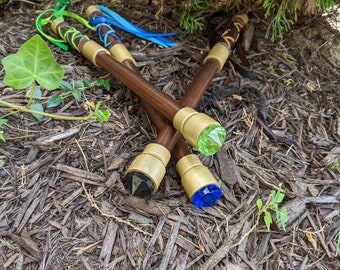 May include: Three wooden staffs with gold-colored tips and different colored gemstone accents. The gemstones are green, black, and blue.
