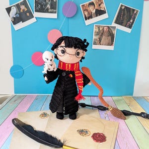 Könnte beinhalten: Gehäkelte Harry Potter-Puppe mit Brille, rotem und gelbem Schal und schwarzem Umhang, die eine weiße Eule hält. Die Puppe ist von thematischen Requisiten umgeben, darunter ein Besen, ein Zauberstab und Briefe mit Wachssiegeln. Blauer Hintergrund mit Fotos und bunten Kreisen.