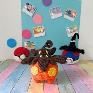 May include: Crocheted Pokémon figures, including an orange and brown creature with yellow spots, a red and white Poké Ball, and a blue and white figure with a black witch hat. The figures are displayed in front of a blue background with photos.