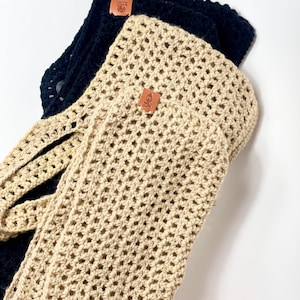 May include: Two crocheted tote bags, one beige and one black, with leather tags. The beige bag is folded on top of the black bag.