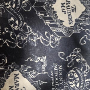 Puede incluir: Tela azul marino con un dise&ntilde;o de mapa ilustrado en blanco. El texto "The Marauder's Map" es visible, junto con otros textos e ilustraciones de edificios y pergaminos. El dise&ntilde;o es un patr&oacute;n repetitivo.