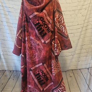 Puede incluir: Una manta con capucha de color burdeos con un patr&oacute;n repetido del sigilo Targaryen y las palabras "Fire and Blood". La manta tambi&eacute;n presenta la frase "Winter is Coming".