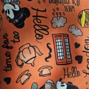 Puede incluir: Tela naranja con ilustraciones de dibujos animados de Mickey Mouse, las palabras "Hello", "time for tea" y "it's raining". El dise&ntilde;o incluye corazones, nubes y una cabina telef&oacute;nica roja. Un dise&ntilde;o divertido y juguet&oacute;n.