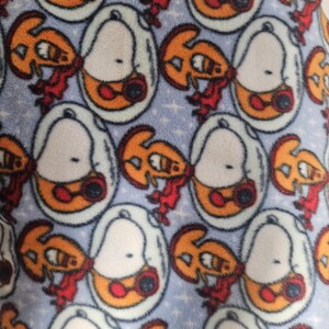 Puede incluir: Tejido polar azul claro con un patr&oacute;n repetido de personajes de dibujos animados. Cada personaje est&aacute; dentro de un &oacute;valo blanco con detalles en naranja y rojo. El fondo tiene un sutil patr&oacute;n de estrellas.