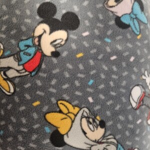 Puede incluir: Tejido polar gris con un patr&oacute;n repetido de Mickey y Minnie Mouse. Los personajes se representan en varias poses, vistiendo sus trajes ic&oacute;nicos, con formas de confeti dispersas en el fondo.