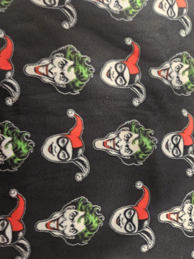 Puede incluir: Tela negra con un patr&oacute;n repetido de las caras de Joker y Harley Quinn. La cara del Joker tiene pelo verde y una amplia sonrisa. La cara de Harley Quinn tiene un sombrero de buf&oacute;n rojo y negro y maquillaje blanco.