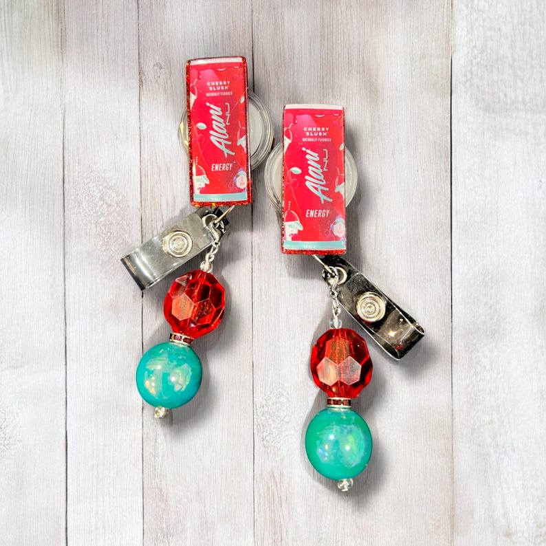 May include: Two red and white Alani Nu energy drink can badge reels with turquoise and red beads.