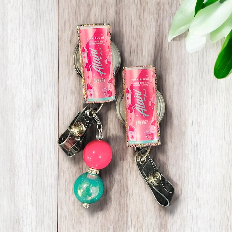 May include: Two pink and gold sparkly keychains with a pink and white can design. The can says "Alani" and "Pink Blush" with a pink and white design. The keychains have a black clip and a pink and turquoise bead.