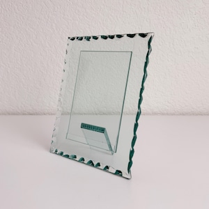 May include: A clear glass picture frame with a rectangular center opening and a decorative scalloped edge featuring a deep green tint. The frame includes a matching glass support stand attached to the back for upright display.