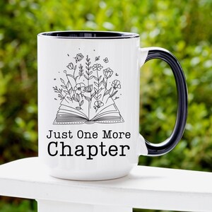 Puede incluir: Taza de caf&eacute; de cer&aacute;mica blanca con borde y asa negros. La taza presenta una ilustraci&oacute;n en blanco y negro de un libro abierto con flores que crecen de &eacute;l. El texto "Just One More Chapter" est&aacute; impreso en negro debajo de la ilustraci&oacute;n.
