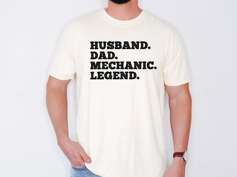 Puede incluir: Una camiseta blanca con texto negro que dice "Husband. Dad. Mechanic. Legend."