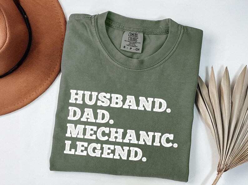 Puede incluir: Una camiseta verde con texto blanco que dice "Husband. Dad. Mechanic. Legend."