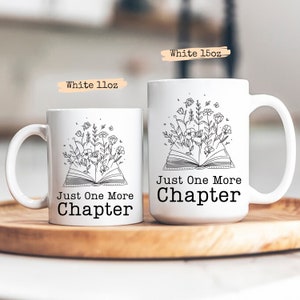 Puede incluir: Dos tazas de cer&aacute;mica blanca con un contorno negro de un libro abierto con flores que salen de &eacute;l. El texto en las tazas dice "Just One More Chapter". Las tazas est&aacute;n sobre una superficie de madera.
