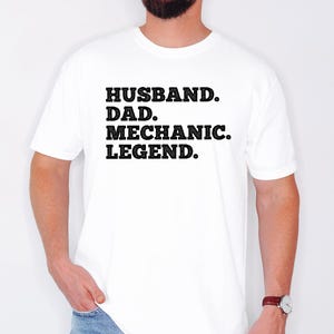 Puede incluir: Camiseta blanca con texto negro que dice "Husband. Dad. Mechanic. Legend."