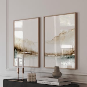 May include: Two framed abstract landscape paintings with brown and blue watercolor washes, displayed on a black console table with candles, a decorative object, and a stack of books. The top book has the text "The Kinfolk Table" on the cover.