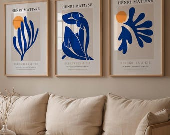 May include: Three framed art prints featuring Henri Matisse designs. Each print has a beige background with a blue abstract shape and an orange circle. The prints are displayed above a beige sofa.