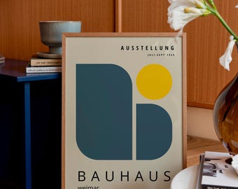Op de afbeelding: Een ingelijste Bauhaus-poster met een beige achtergrond. De poster toont een grote, donkerblauwe vorm, een gele cirkel en het woord "BAUHAUS" in zwart. De tekst "AUSSTELLUNG JULI-SEPT 1923" is ook zichtbaar.