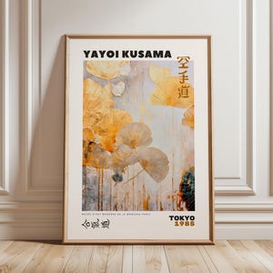 Puede incluir: Impresión artística enmarcada de una obra de Yayoi Kusama. La impresión muestra formas abstractas en tonos amarillos y beige sobre un fondo texturizado. El texto incluye "YAYOI KUSAMA", caracteres japoneses y "TOKYO 1985". La obra de arte se presenta en un marco de madera.