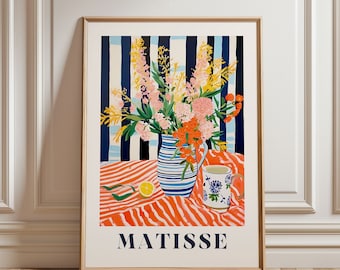 May include: A framed art print featuring a still life with a vase of flowers, a patterned mug, and a lemon slice. The background has blue and white stripes, and the table has an orange and white striped pattern. The word "MATISSE" is at the bottom.