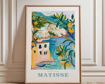 May include: A framed art print featuring a coastal scene with buildings, water, and trees with oranges. The print is titled "MATISSE" with "AMALFI COAST" below. The artwork is in a gold frame and leans against a white wall.