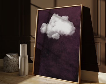 Op de afbeelding: Een ingelijste print van een enkele witte wolk tegen een donkerpaarse achtergrond. De lijst is goudkleurig en de print hangt aan een muur.