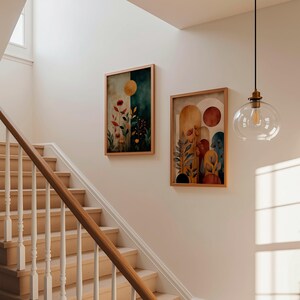 Puede incluir: Dos pinturas en acuarela enmarcadas con temas bot&aacute;nicos cuelgan de una pared. Las pinturas presentan colores c&aacute;lidos, incluyendo naranja, rojo y verde, con dise&ntilde;os florales abstractos. Tambi&eacute;n se ven una escalera de madera y una l&aacute;mpara colgante de cristal.