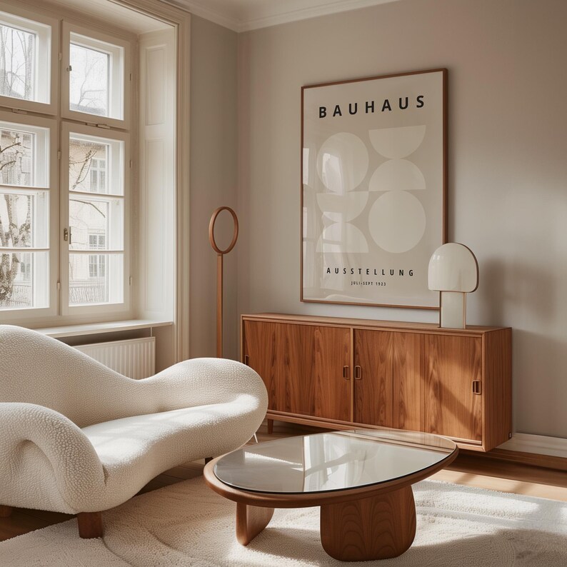 May include: A modern living room with a white sofa, a wooden coffee table, and a wooden cabinet. A framed Bauhaus poster hangs on the wall above the cabinet. A white lamp sits on the cabinet. A wooden floor lamp stands near the cabinet.