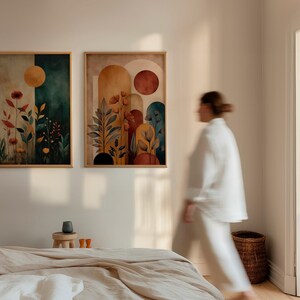 Puede incluir: Dos impresiones art&iacute;sticas en acuarela enmarcadas. Una presenta un fondo verde oscuro y beige con un sol amarillo y flores rojas. La otra tiene un fondo beige y naranja con formas de arco y flores rojas. Ambas est&aacute;n en marcos de madera clara.