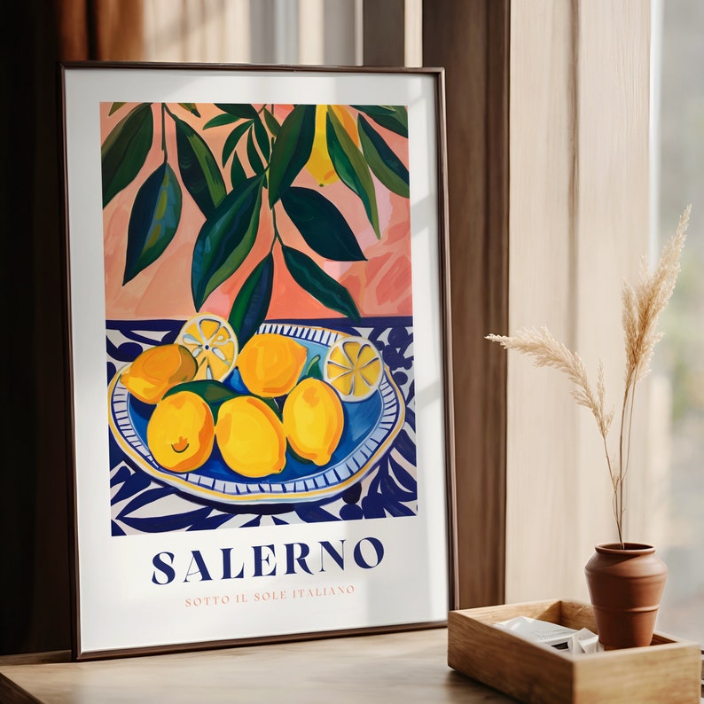 May include: A framed print with a colorful illustration of lemons on a blue and white patterned plate. The background features green leaves and a pink and peach color scheme. The text "SALERNO SOTTO IL SOLE ITALIANO" is at the bottom of the print.
