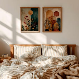 Puede incluir: Dos impresiones art&iacute;sticas bot&aacute;nicas enmarcadas con tonos c&aacute;lidos cuelgan sobre una cama con ropa de cama a rayas. La obra de arte presenta dise&ntilde;os florales abstractos con elementos de sol y arco. La cama tiene un marco de madera y una manta marr&oacute;n.