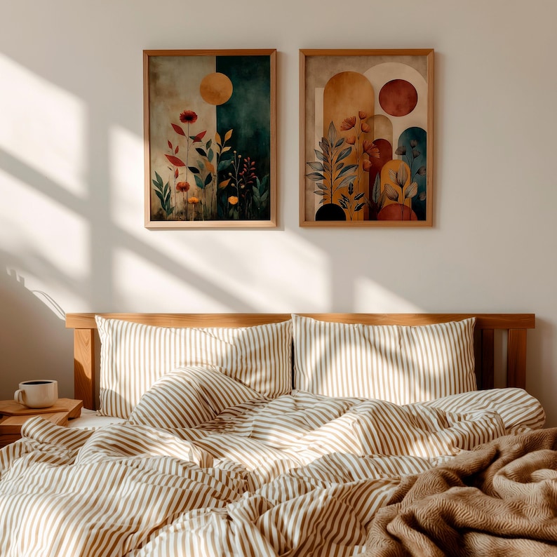 Puede incluir: Dos impresiones art&iacute;sticas bot&aacute;nicas enmarcadas con tonos c&aacute;lidos cuelgan sobre una cama con ropa de cama a rayas. La obra de arte presenta dise&ntilde;os florales abstractos con elementos de sol y arco. La cama tiene un marco de madera y una manta marr&oacute;n.